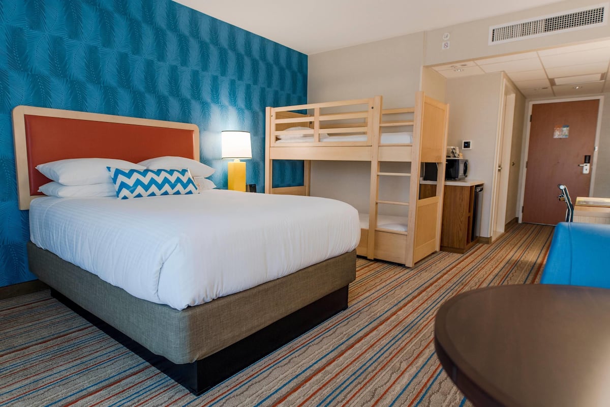A hotel room with a large bed, a bunk bed, a desk, and a chair.