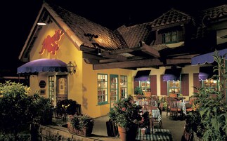 A traditional building with a tiled roof, multiple windows, and outdoor seating area with tables and chairs.