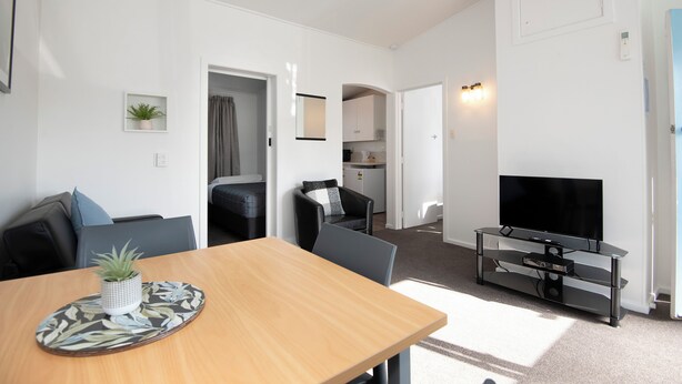 A modern living room with a wooden dining table, a flat-screen TV, and a seating area with a sofa and chairs. - Spanish Lady Motel (Napier)