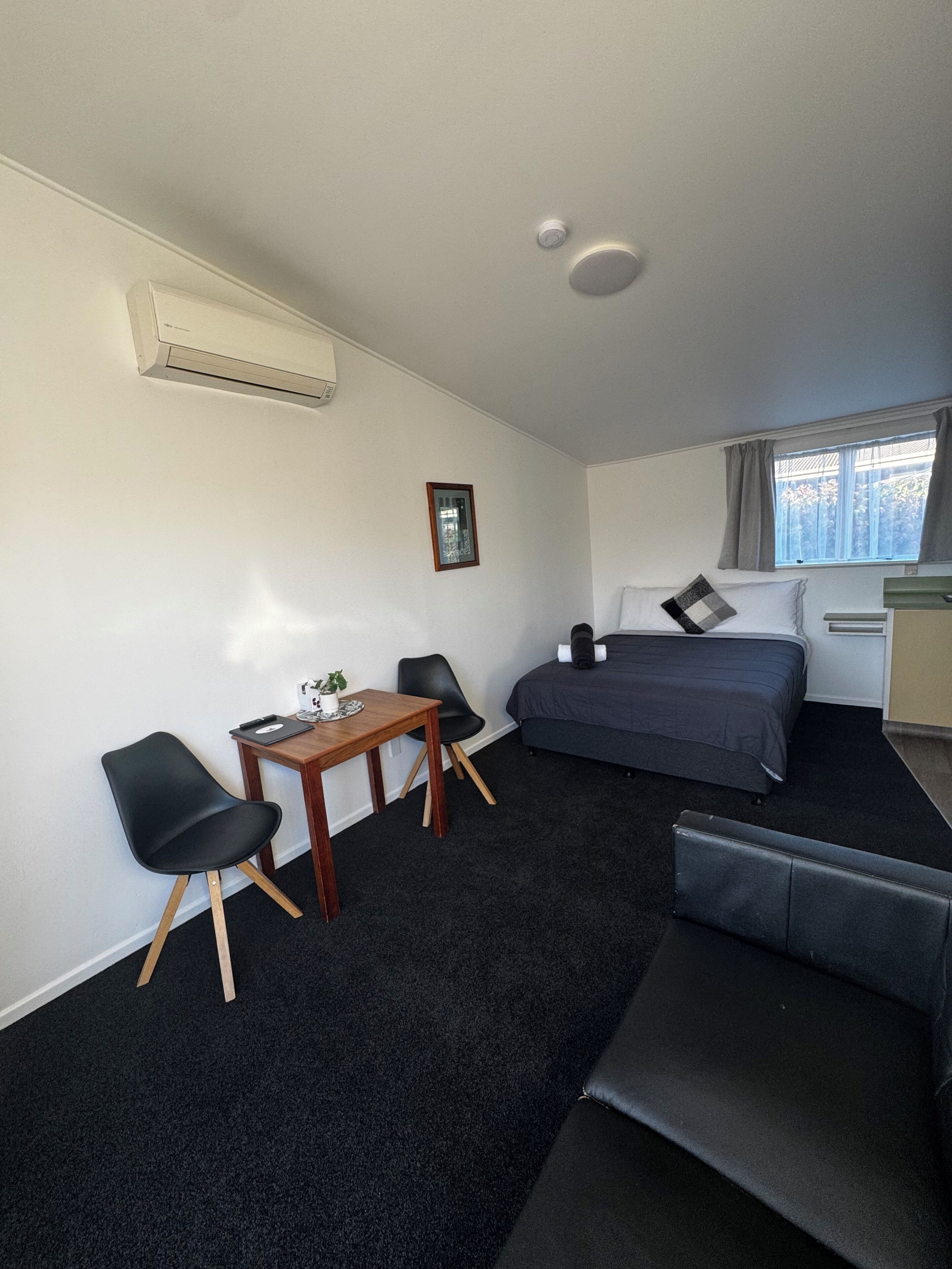 Una habitación de hotel compacta con cama, un escritorio pequeño con silla, un sofá y una ventana con cortinas.
