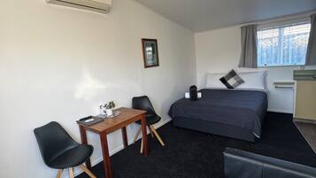 Una habitación de hotel compacta con cama, un escritorio pequeño con silla, un sofá y una ventana con cortinas.