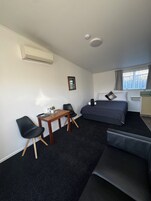 Una habitación de hotel compacta con cama, un escritorio pequeño con silla, un sofá y una ventana con cortinas.