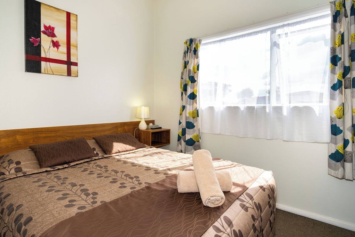 A hotel room with a bed, a nightstand, a lamp, and a window with curtains.