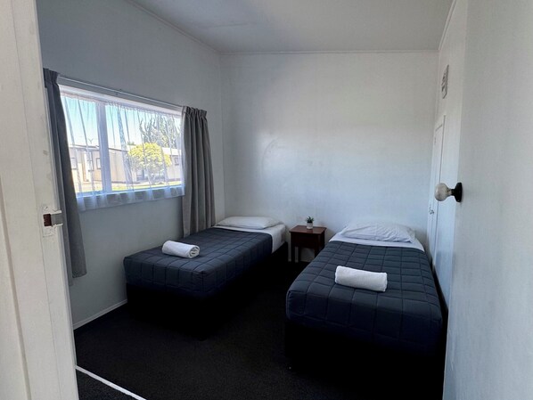 A small, single-room accommodation with two beds, a window, a small table, and a door.