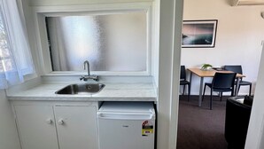 A compact kitchen with a sink, a small refrigerator, and a dining area with a table and chairs. - Spanish Lady Motel (Napier)