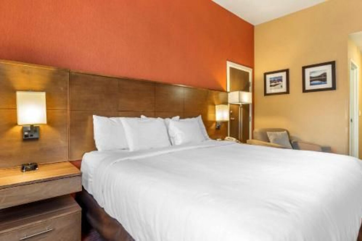 A hotel room with a large bed, two bedside tables with lamps, a wooden headboard, and two framed pictures on the wall.