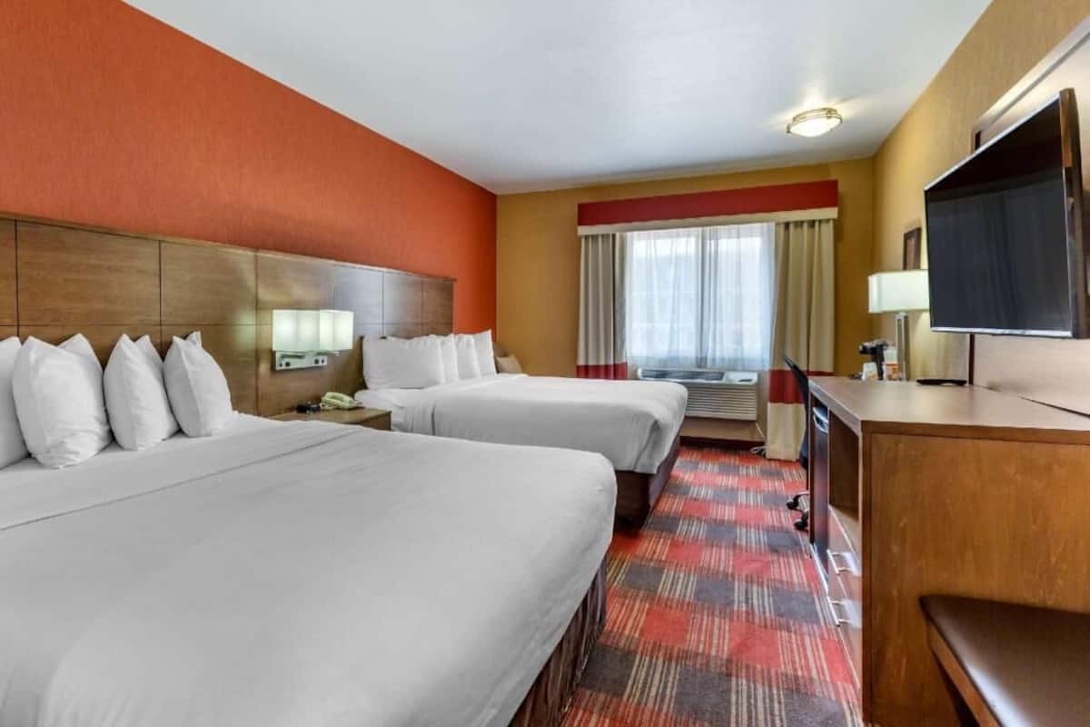 Een hotelkamer met twee bedden, een bureau, een televisie en een raam met gordijnen.