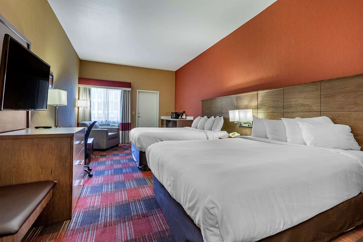 A hotel room with two beds, a desk, a TV, and a window with curtains.