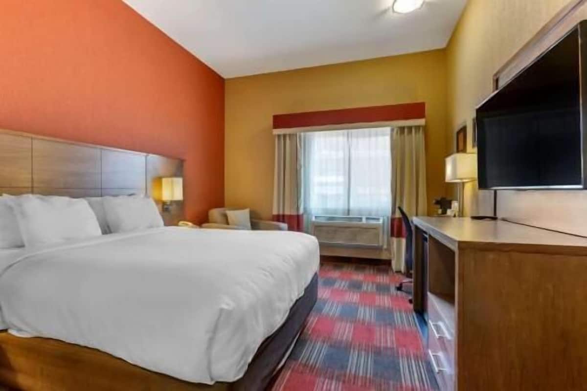A hotel room with a large bed, a desk, a TV, and a window with curtains.