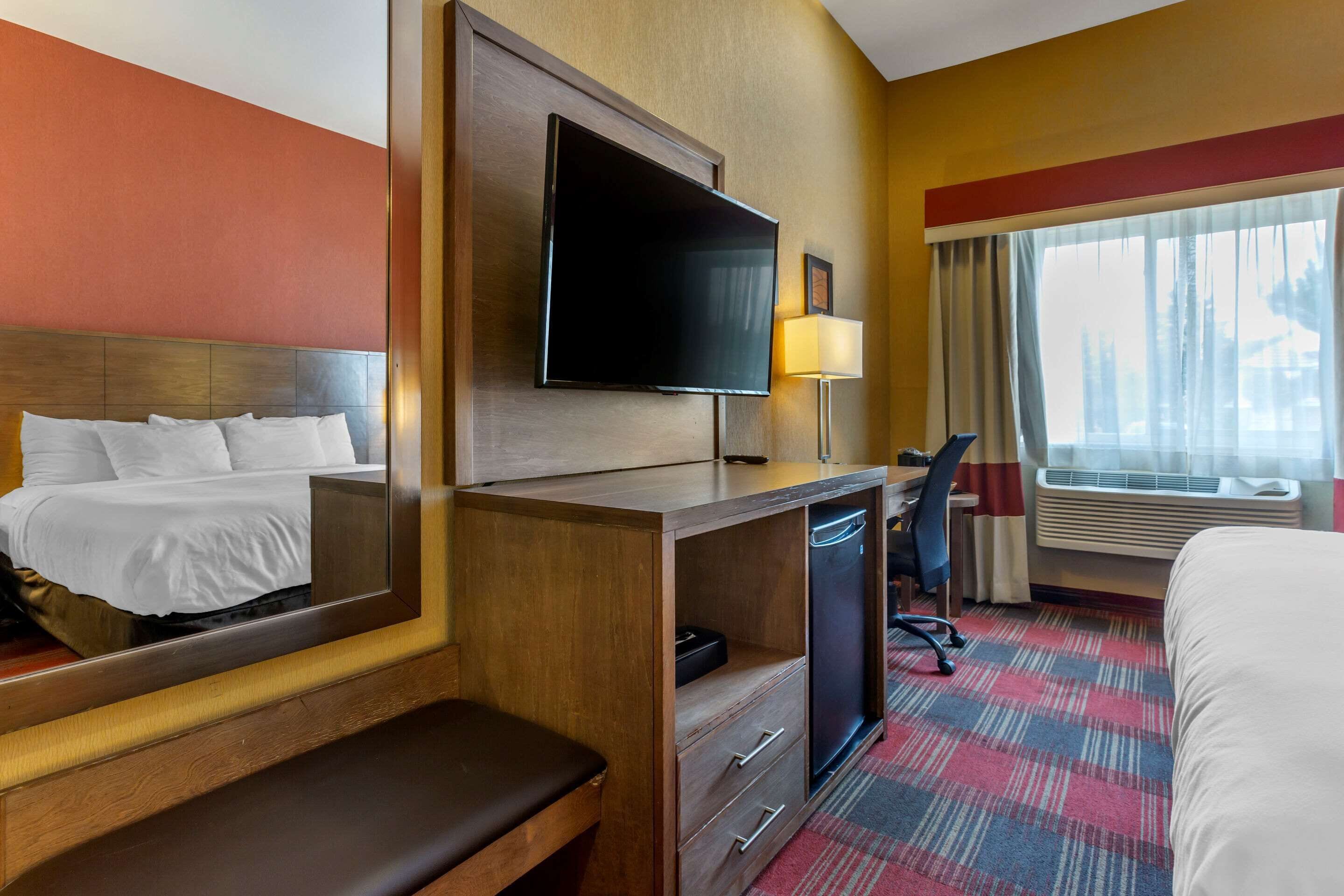 A hotel room with a bed, a desk with a chair, a television, a lamp, and a window with curtains.