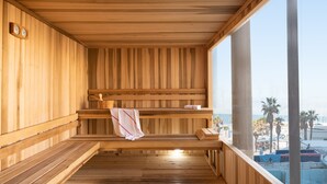 Una sauna de madera con bancos, un perchero para toallas y vistas a la playa y palmeras.