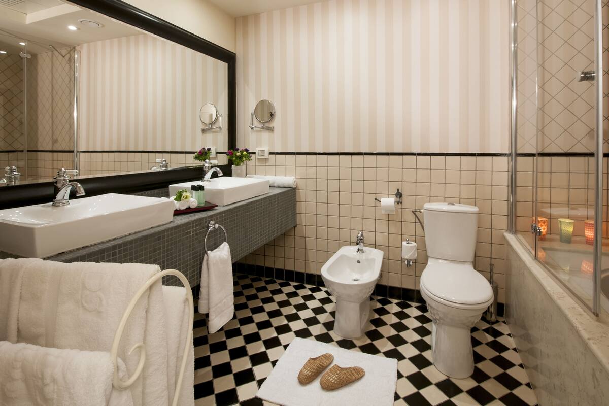 A bathroom with a checkered floor, a large mirror, a bathtub, a bidet, and a toilet.