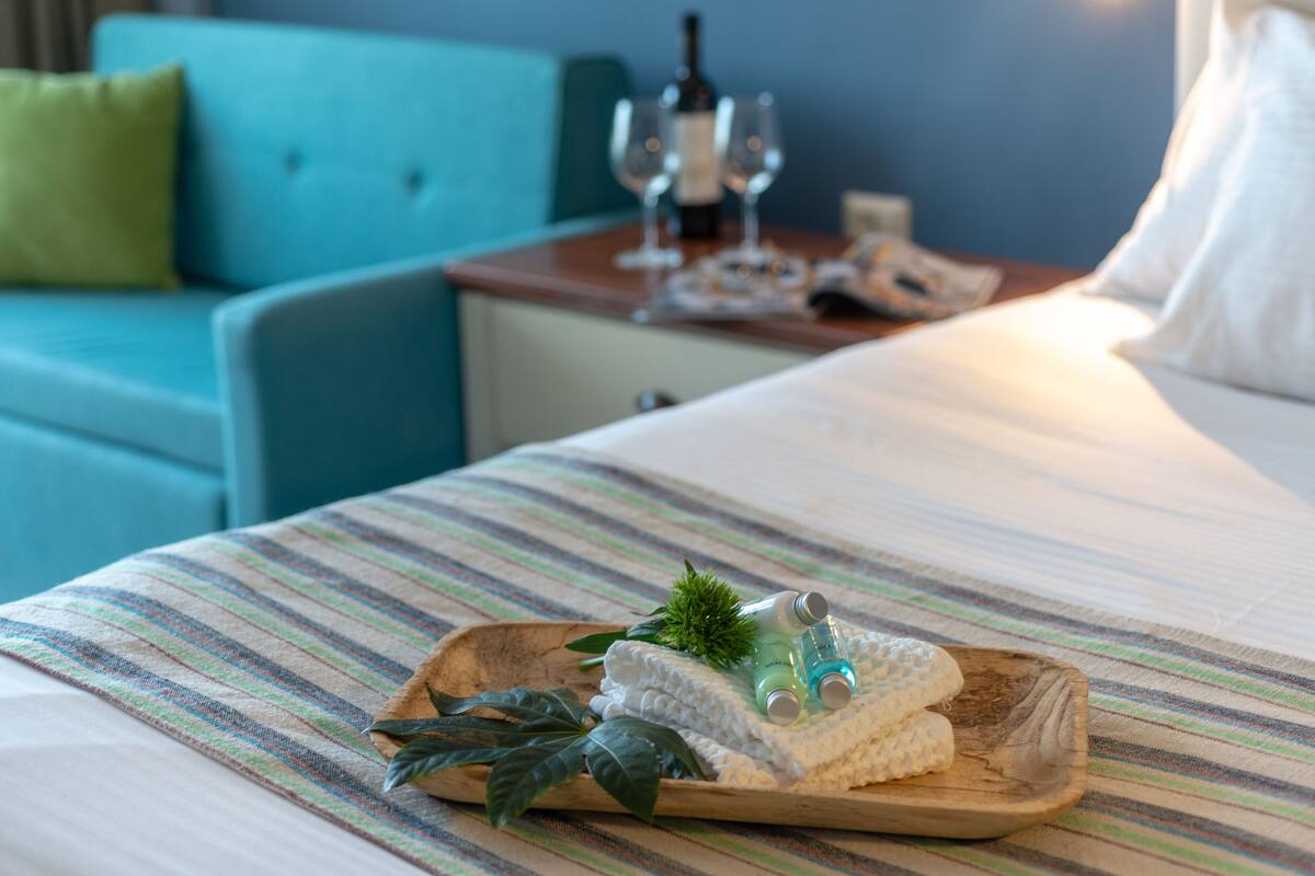 A hotel room with a bed, a wooden side table, a blue sofa, and a striped bedspread.
