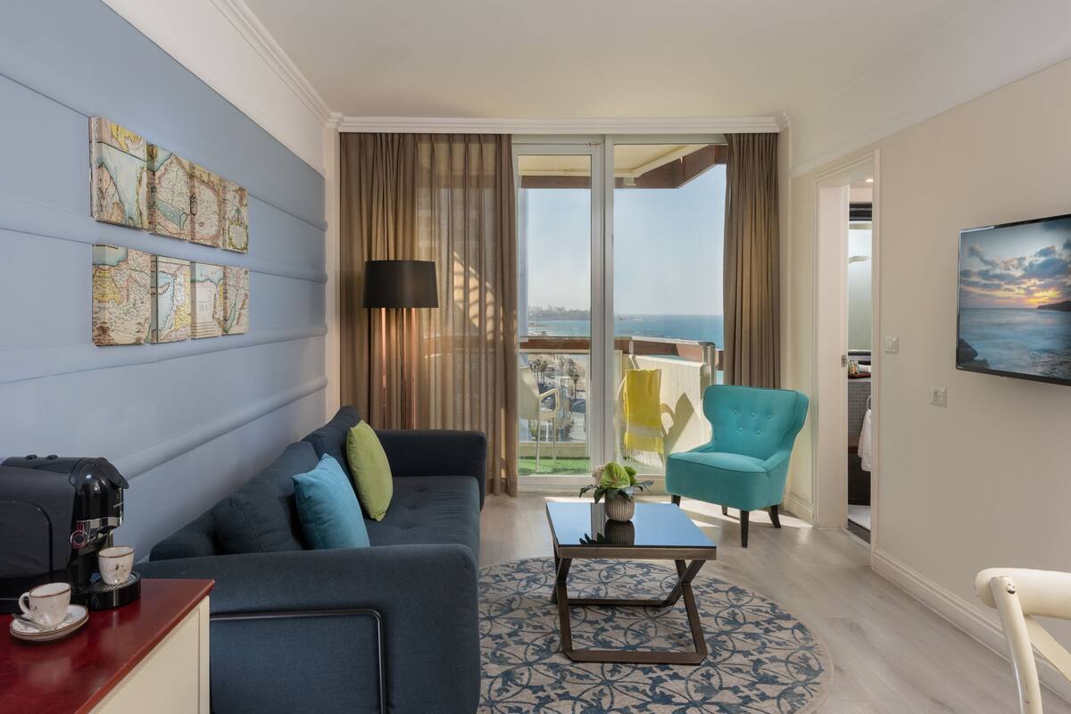 A modern hotel room with a balcony, a sofa, a coffee table, and a TV.