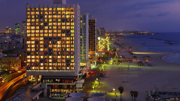 Un hotel de gran altura con varios pisos, ubicación frente a la playa y un paseo marítimo bien iluminado.