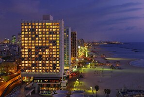 Un hotel de gran altura con varios pisos, ubicación frente a la playa y un paseo marítimo bien iluminado.