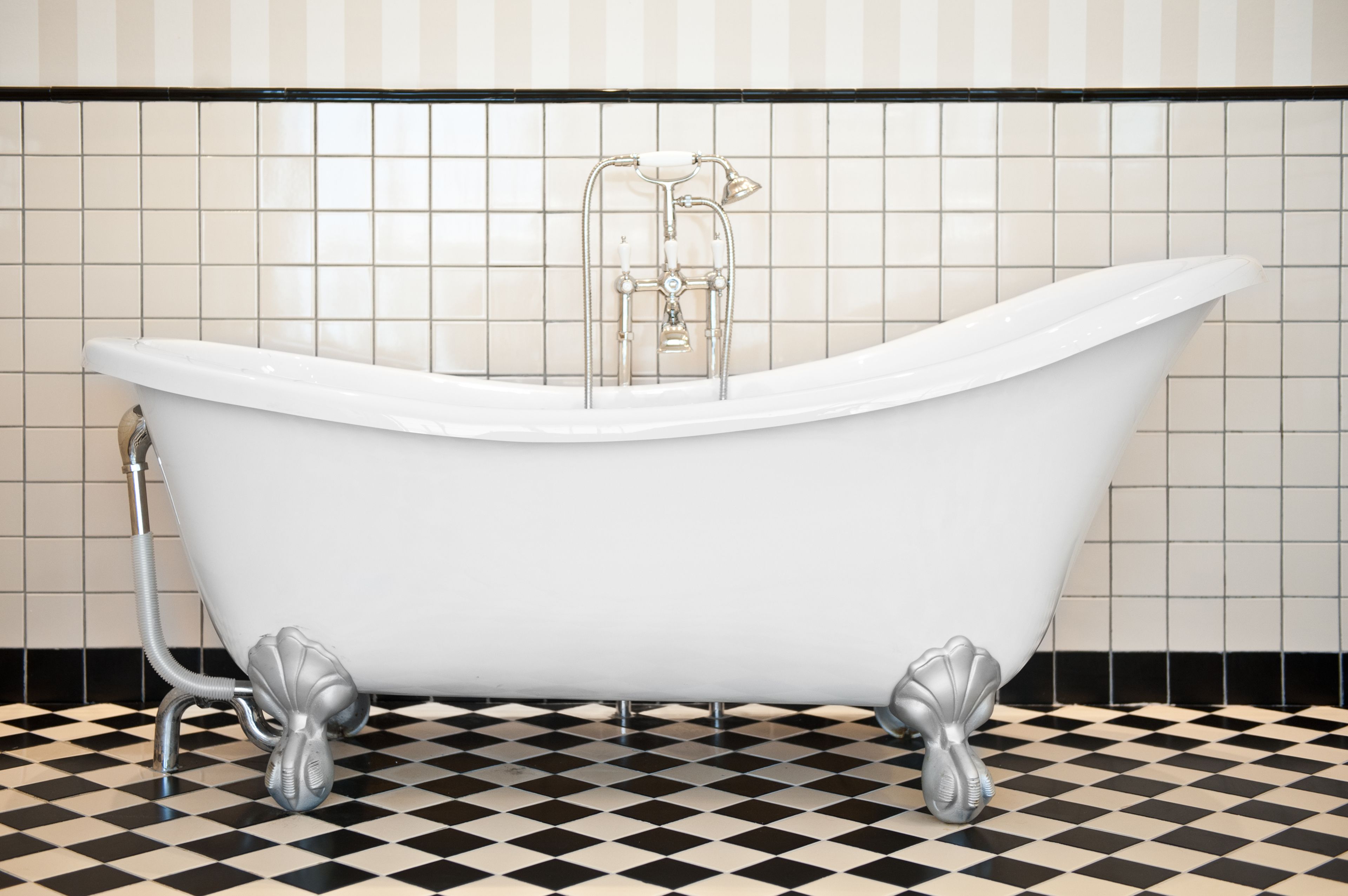 A white freestanding bathtub with claw feet, a showerhead, and a handheld shower attachment, set against a tiled wall and floor.