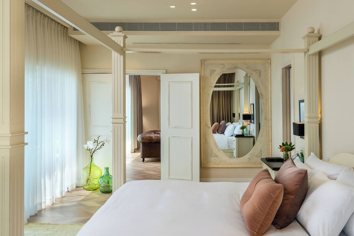 A spacious bedroom with a large bed, a mirror, and a view of a bathroom.