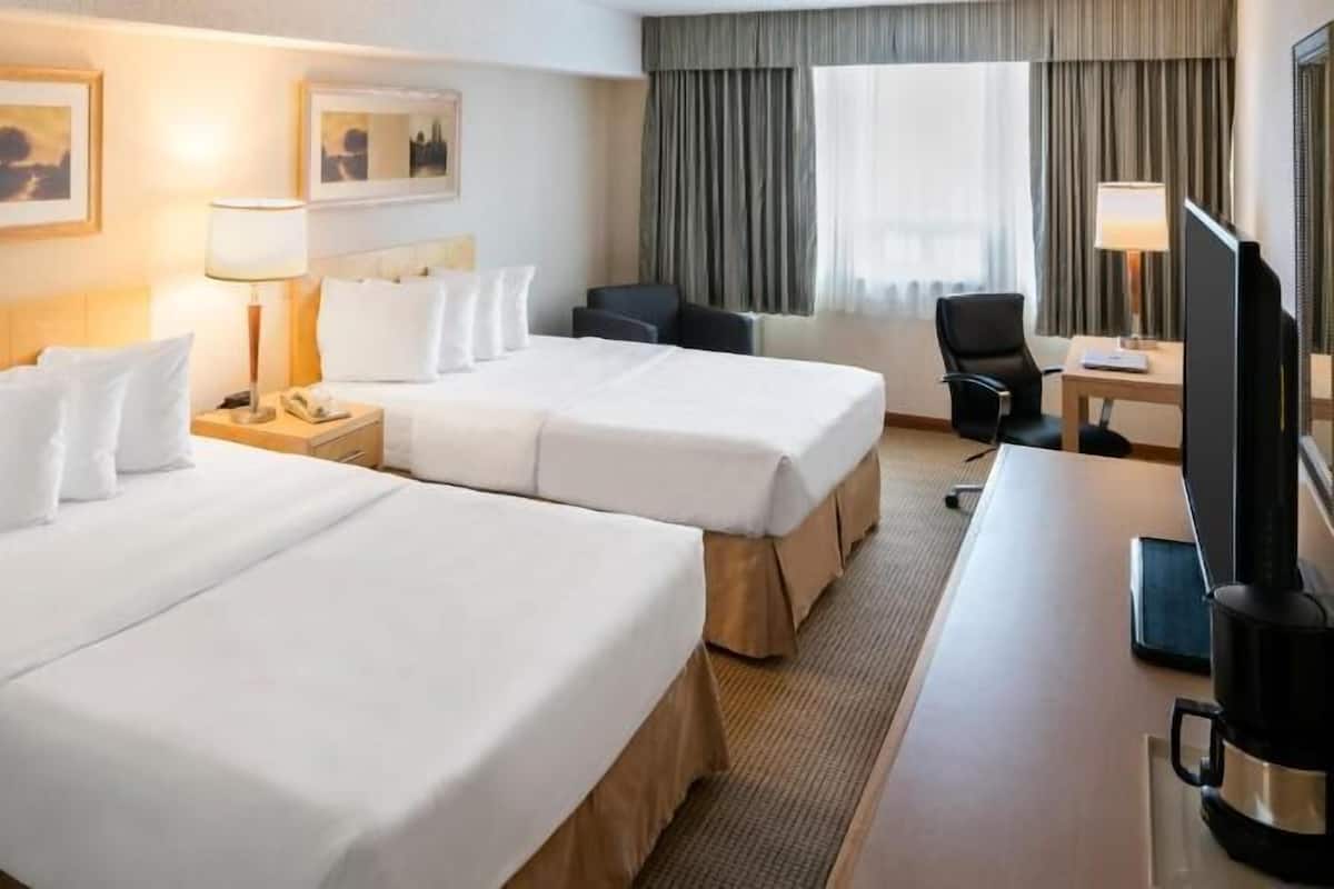 Ein Hotelzimmer mit zwei Betten, einem Schreibtisch, einem Sessel, einem Fernseher und Bildern an der Wand.