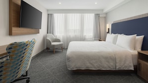 Een hotelkamer met een bed, een stoel, een televisie en een raam met gordijnen.