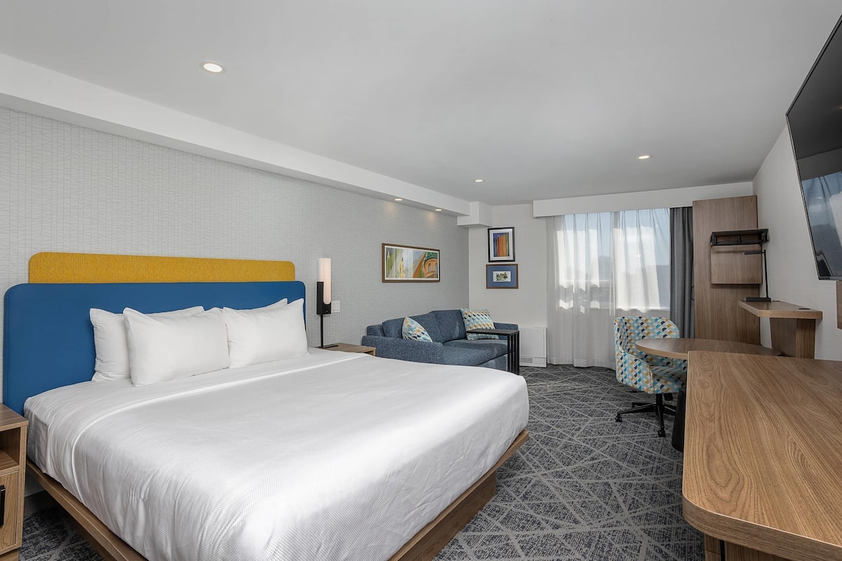 Ein Hotelzimmer mit einem großen Bett, einem Schreibtisch, einem Stuhl und einem Fernseher.