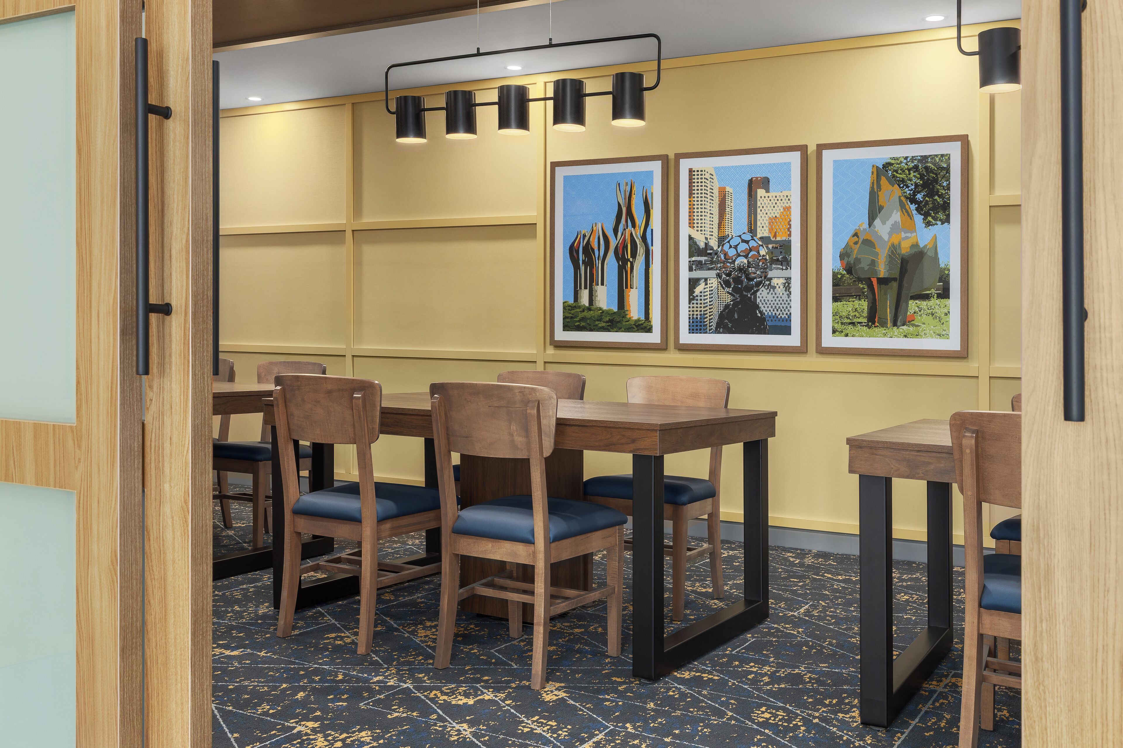 A dining area with wooden tables and chairs, a patterned floor, and framed artwork on the wall.