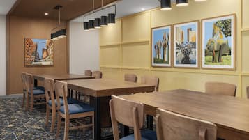 Un salón de conferencias con mesas y sillas de madera, lámparas colgantes negras y cuadros en las paredes.