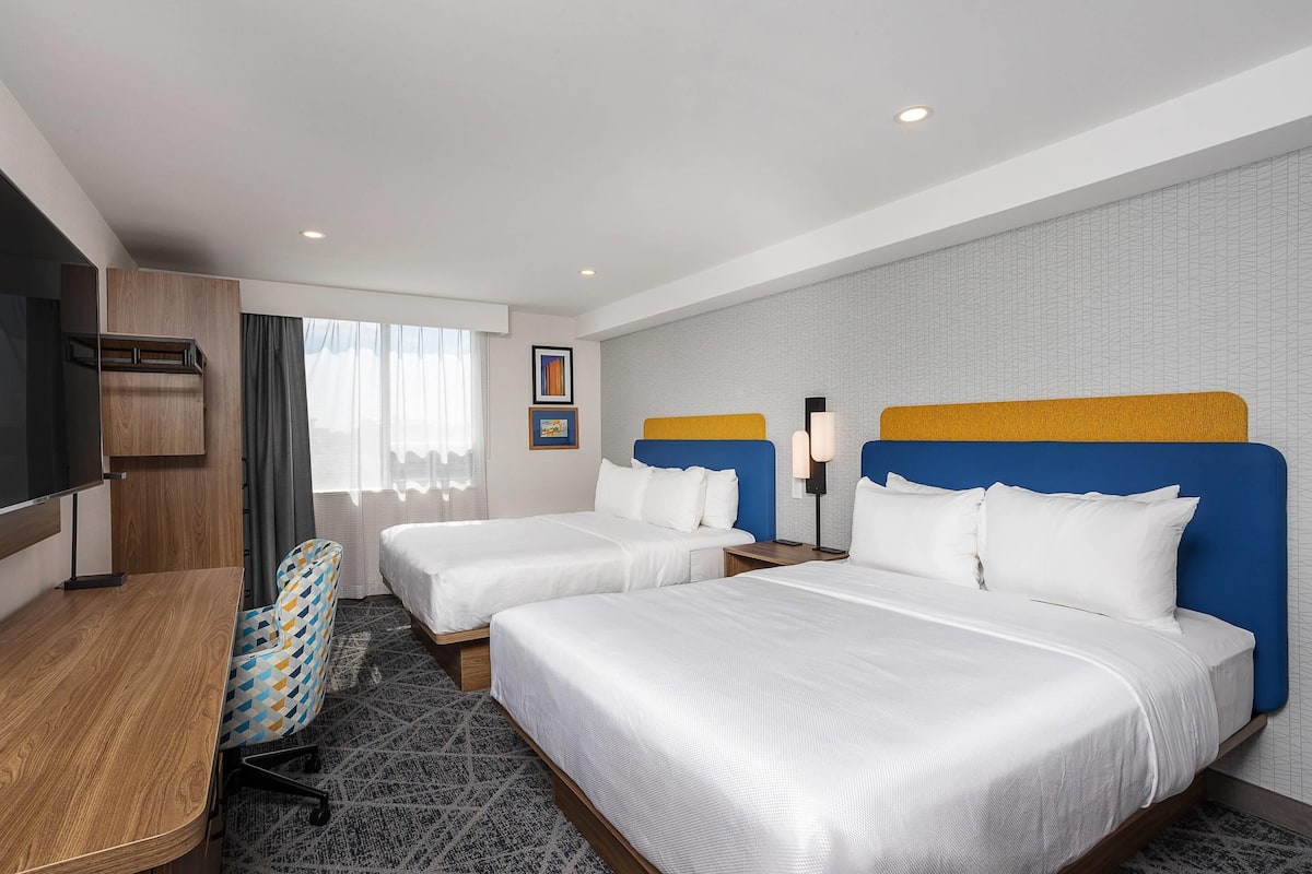 Ein Hotelzimmer mit zwei Betten, einem Schreibtisch, einem Stuhl und einem Fernseher.