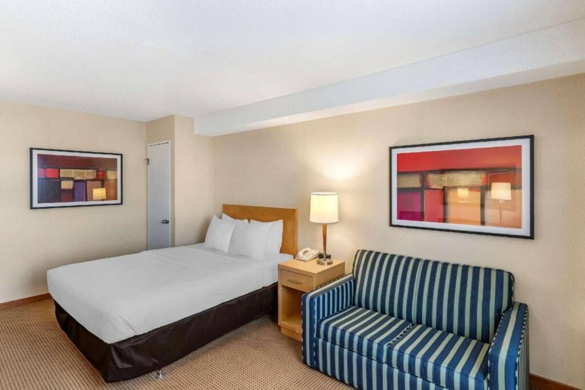 Ein Hotelzimmer mit einem Bett, einem Nachttisch mit Lampe, einer gestreiften Couch und zwei gerahmten abstrakten Bildern an den Wänden.