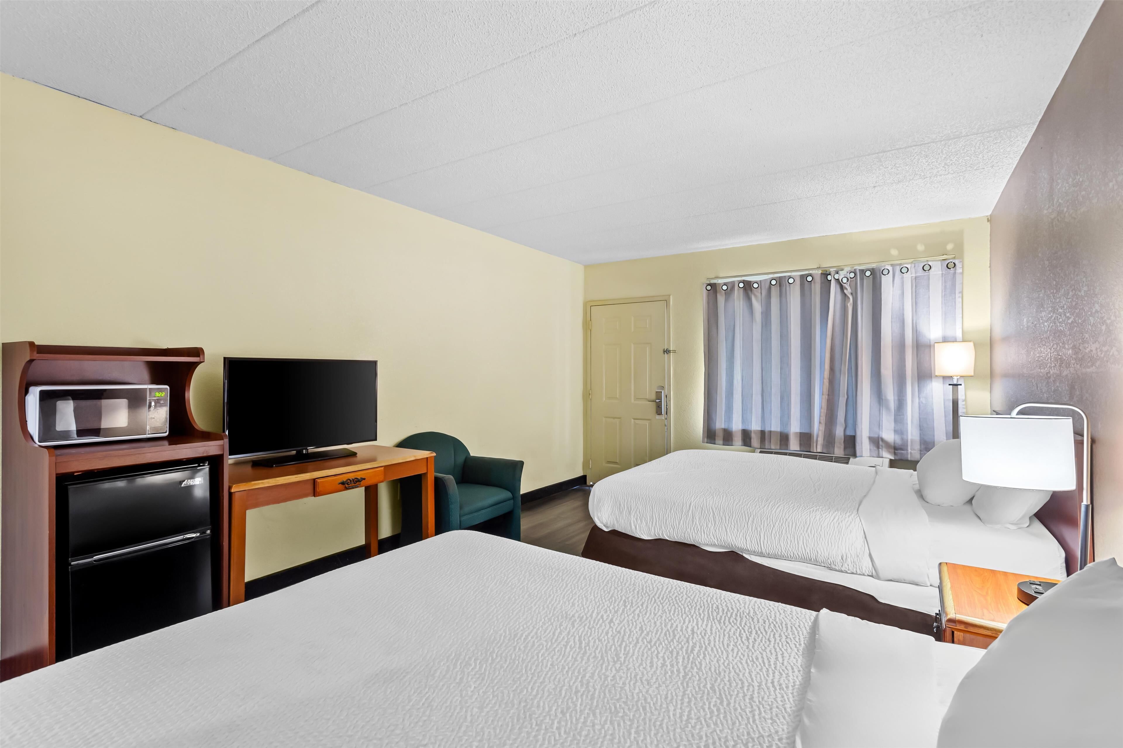A hotel room with two beds, a TV, a refrigerator, a desk, and a window with curtains.