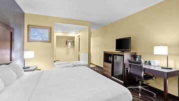 A hotel room with a large bed, a desk with a chair, a television, a desk lamp, and a bathroom visible through an open door.