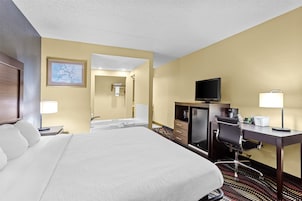 Habitación de hotel con una cama grande, un escritorio con silla, televisión, lámpara de escritorio y un baño visible a través de una puerta abierta.
