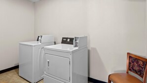 A laundry room with two white washers and dryers, a brown chair, and a tiled floor.