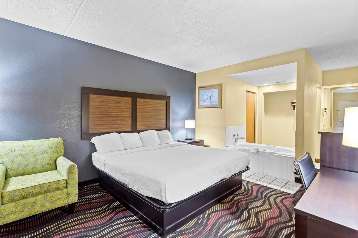A hotel room with a bed, a chair, a desk, a bathroom with a bathtub, and a mirror.