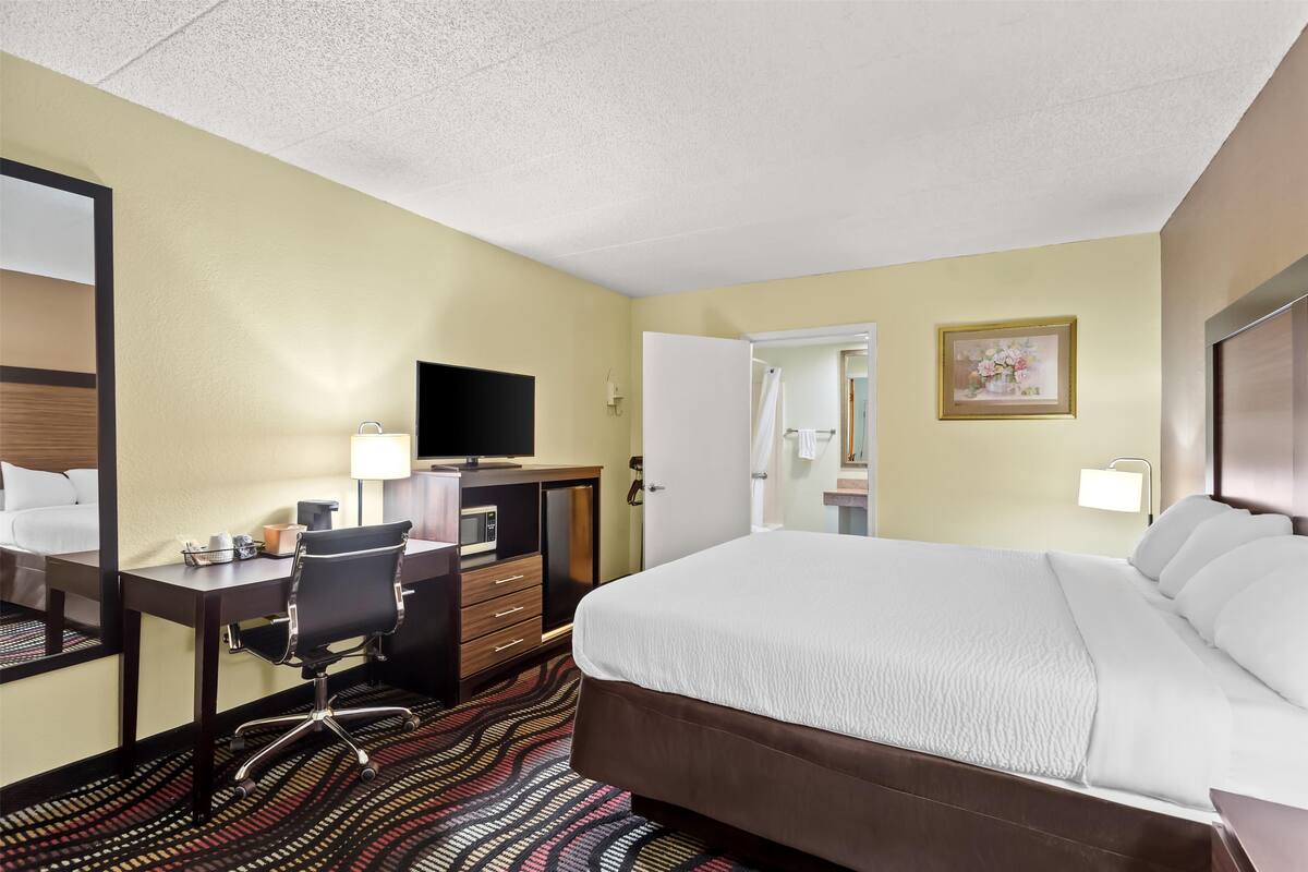 A hotel room with a bed, desk, chair, television, and a bathroom door.