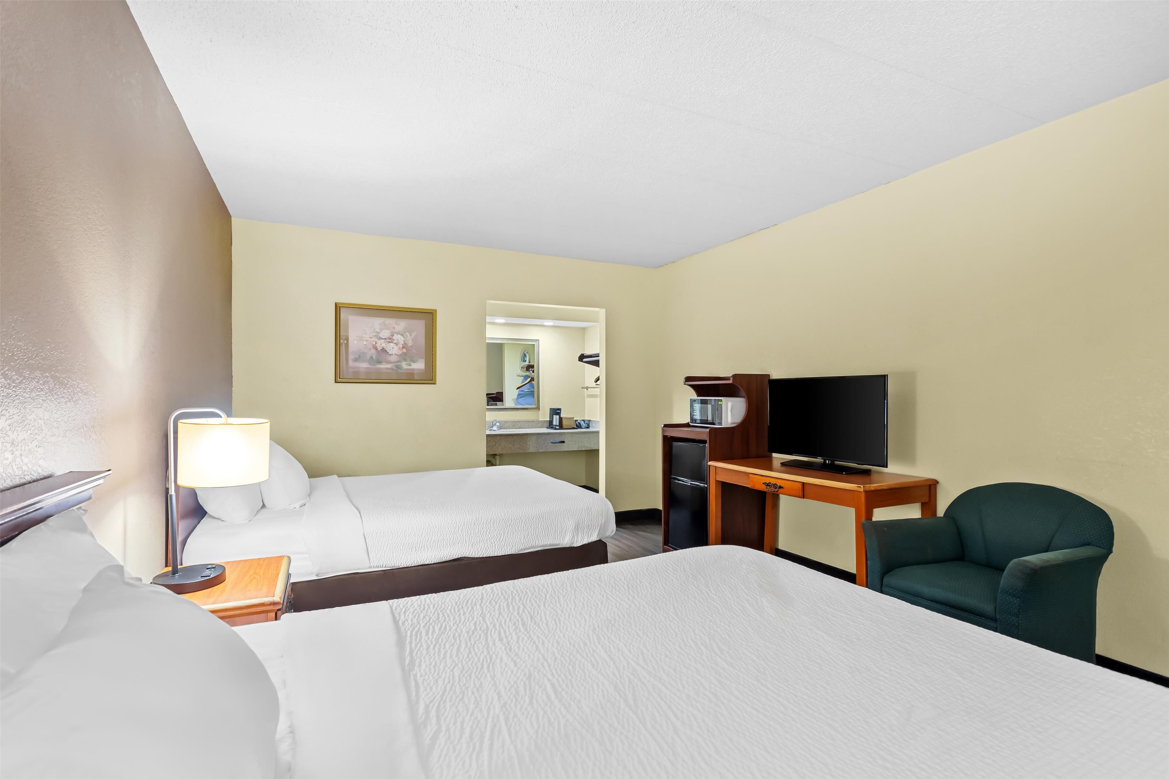 A hotel room with two beds, a desk with a television, a chair, and a bathroom visible through an open door.