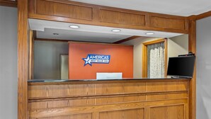 A reception desk with a wooden finish, a sign for Amerias Best Value Inn, and a flat-screen TV on the right.