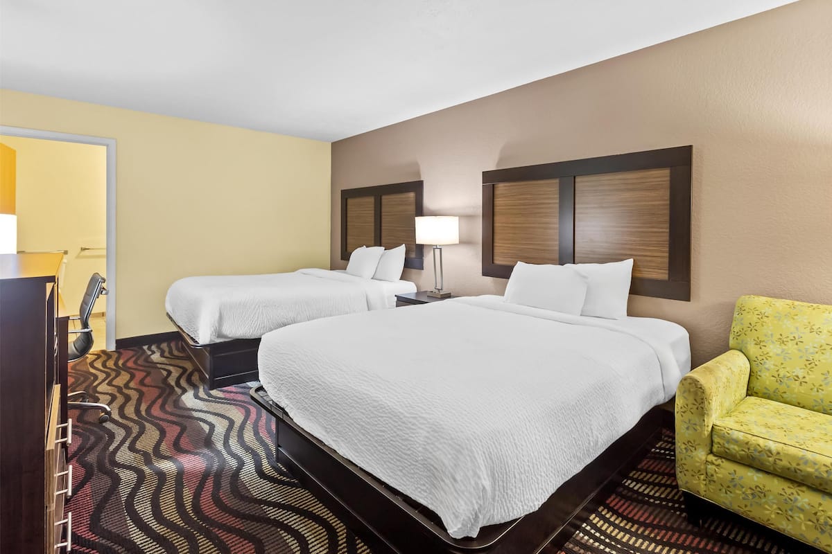 A hotel room with two beds, a desk, a chair, and a patterned carpet.