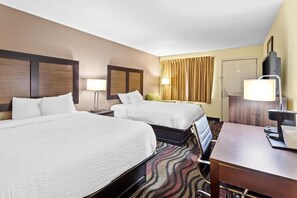 Two single beds with white linens and dark headboards, a desk, and a television.