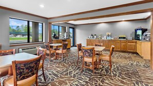 A hotel room with a dining area, kitchen, and large windows offering a view of the outdoors.