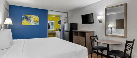 A hotel room with a bed, a desk with a chair, a TV, and a painting on the wall.
