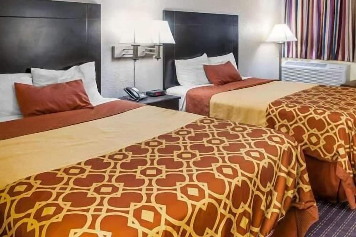 Una habitación de hotel con dos camas, una mesita de noche con teléfono y una ventana con cortinas.