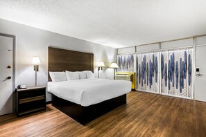 Una habitación de hotel con una cama grande, mesitas de noche con lámparas, un armario y suelo de madera.