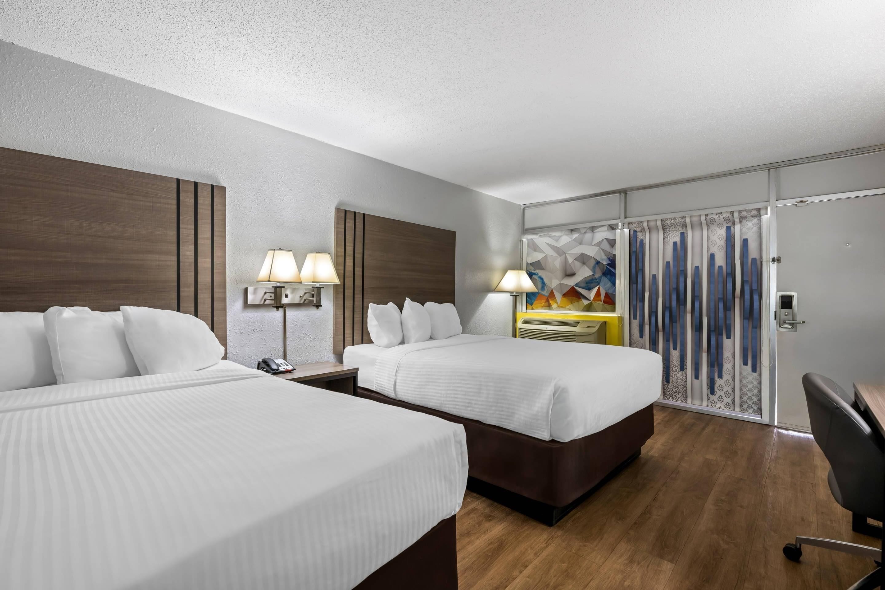 A hotel room with two beds, a desk, a chair, and a bathroom with a shower curtain.