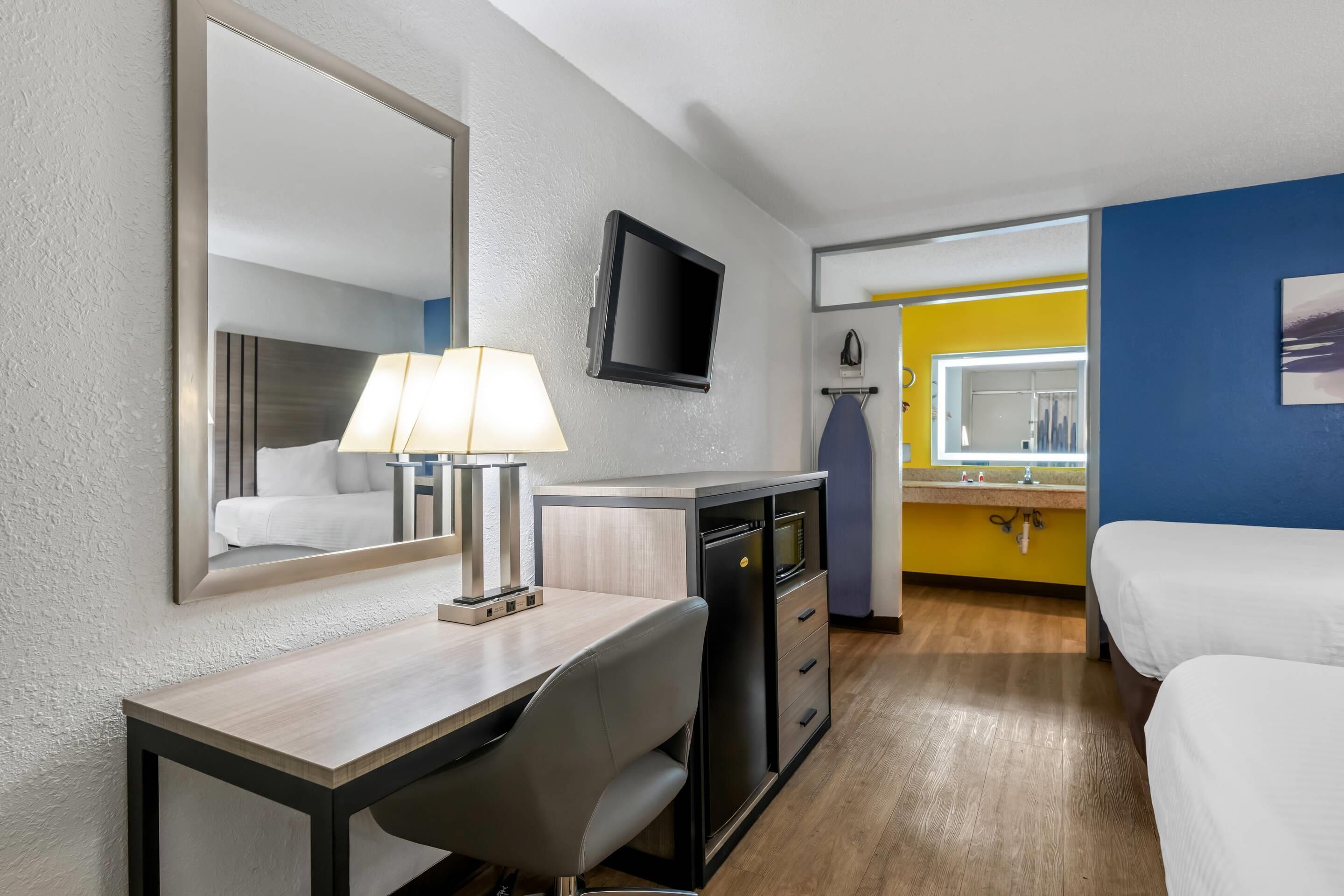 Habitación de hotel con escritorio, silla, cama, televisión y espejo.