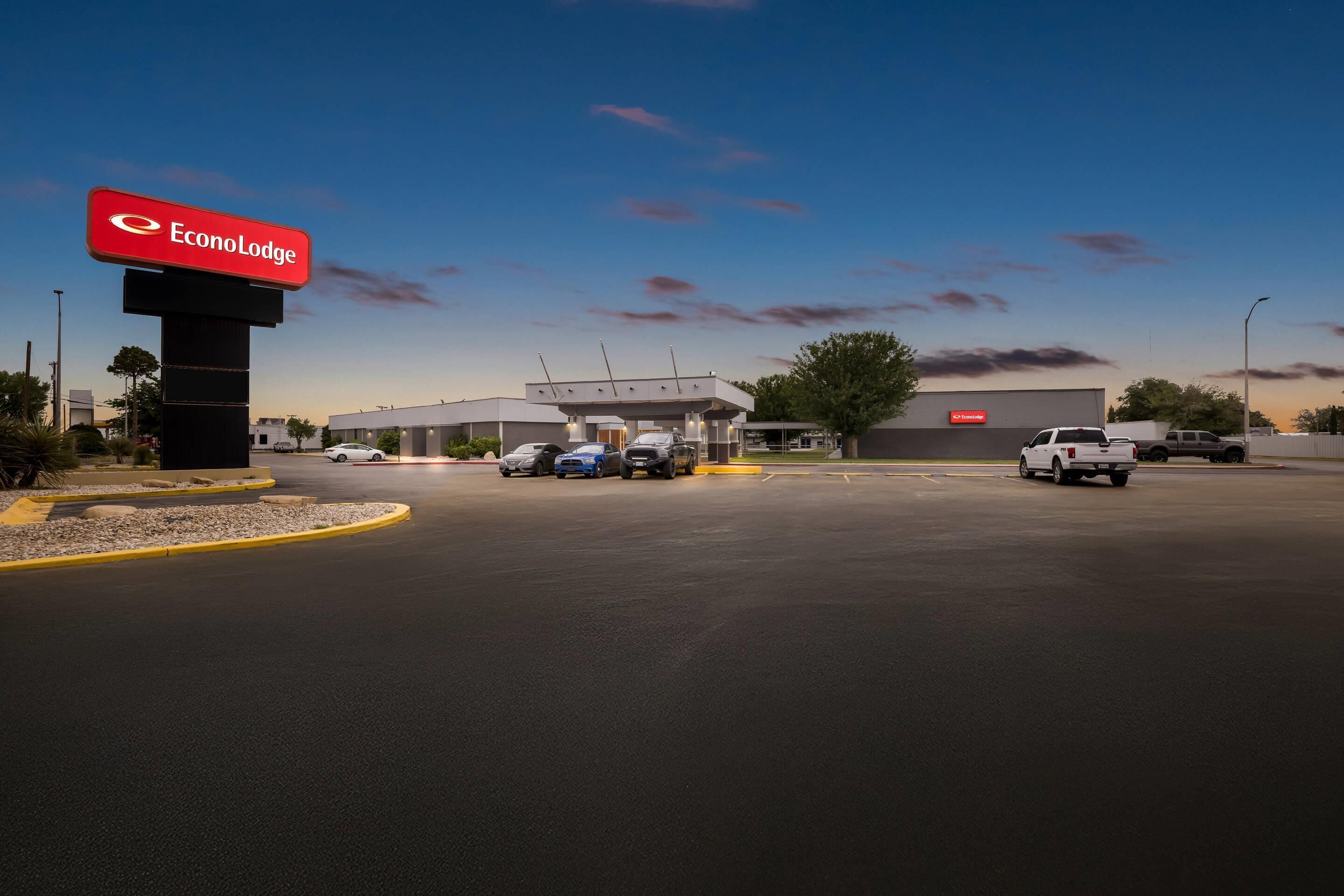 Un vaste parking agrémenté d’un grand panneau indiquant l’établissement EconoLodge, un bâtiment moderne et plusieurs véhicules stationnés.