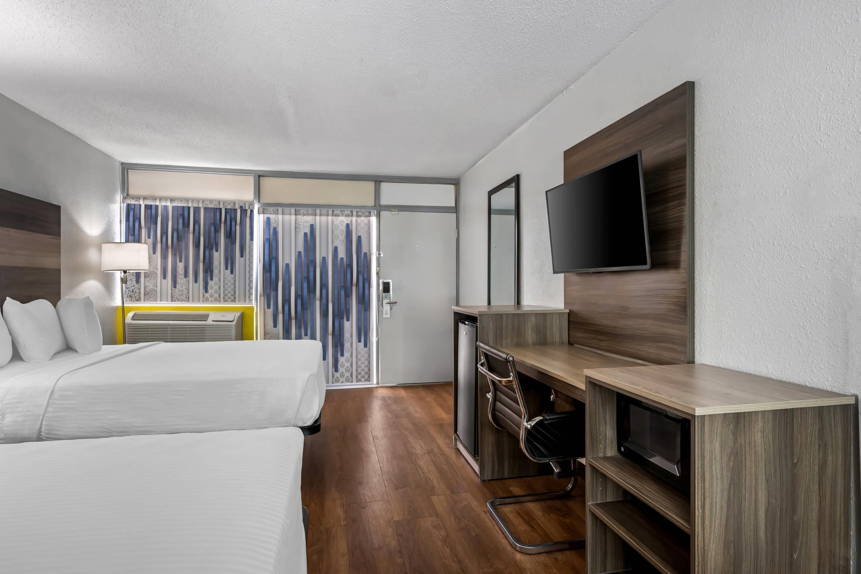 Habitación de hotel con dos camas, un escritorio con televisor, lámpara de escritorio y ventana con cortinas.