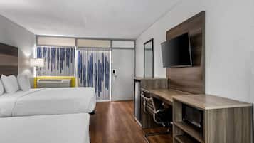 Een hotelkamer met twee bedden, een bureau met een televisie, een bureaulamp en een raam met gordijnen.