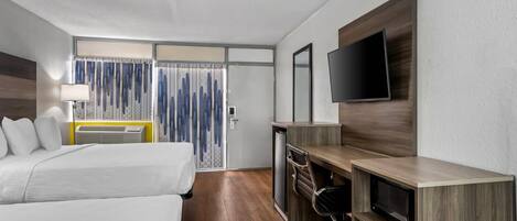 Habitación de hotel con dos camas, un escritorio con televisor, lámpara de escritorio y ventana con cortinas.