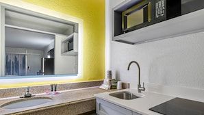 Un baño moderno con encimera de granito, un lavamanos, un espejo, un microondas y un dispensador de toallas.